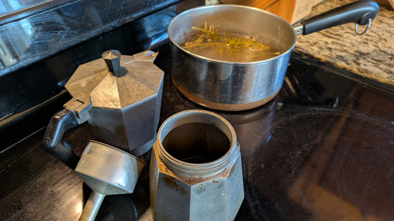 A disassembled moka pot sits next to a stovetop simmer pot filled with evergreen cuttings.