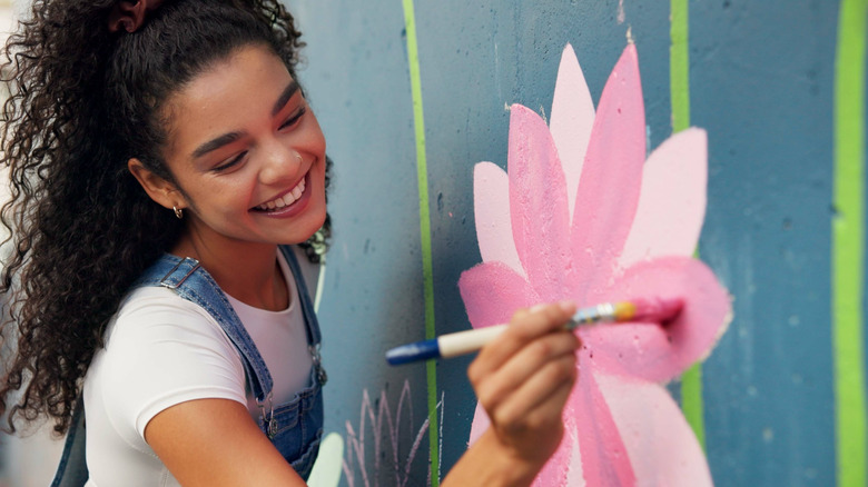 Woman smiling and painting a flower on a wall