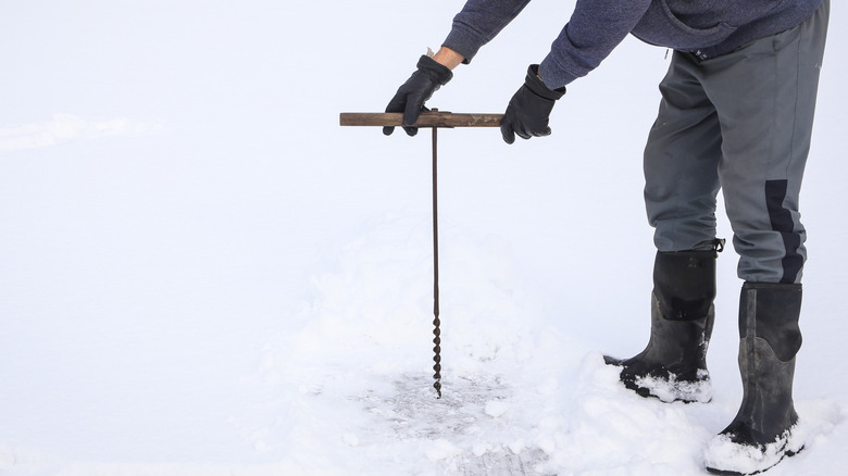 A man drilling into a frozen lake with a manual auger