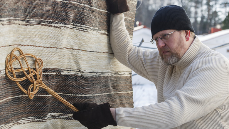 A man using a wood carpet beater.