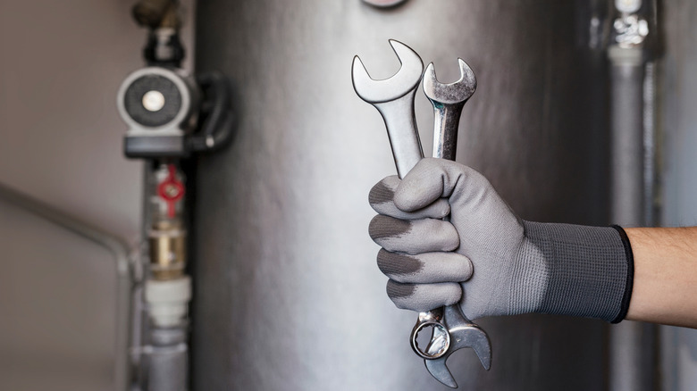 A gloved hand holding two wrenches in front of a heater