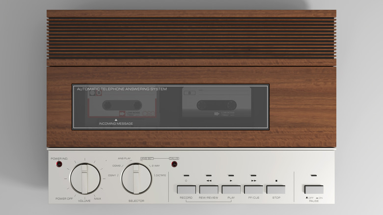 A vintage telephone answering system with a metal and faux wood case holding analog tapes.