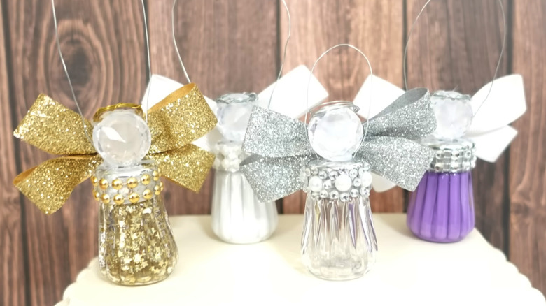 Four salt and pepper shaker angels in gold, white, silver, and purple on a white table with a wood panel background.