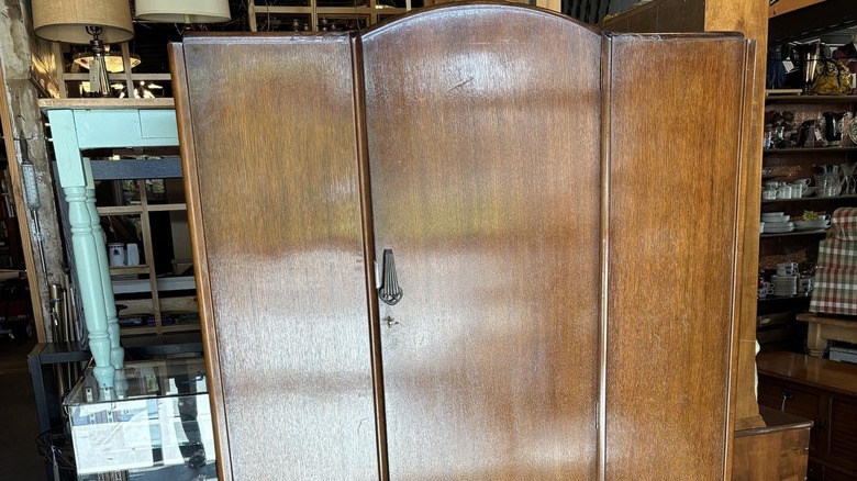 Art deco armoire with simple, smooth wood panels in a thrift-store setting.
