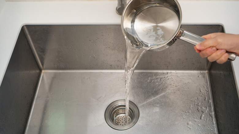 hand pouring boiling water from a stainless steel pot down a kitchen drain