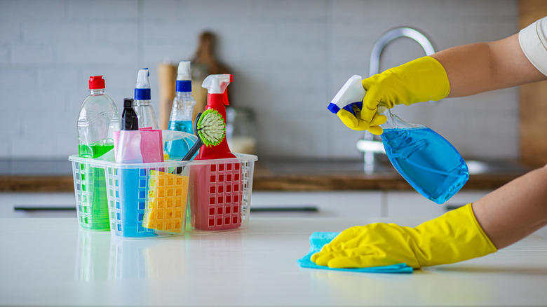 Person spraying and wiping counter next to filled cleaning caddy