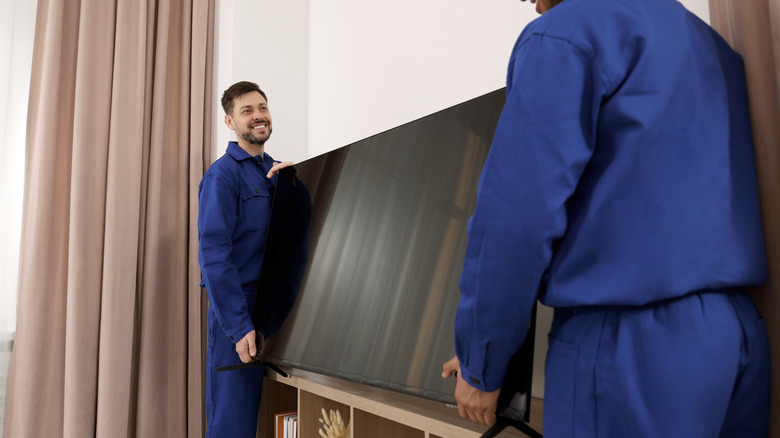 Technicians installing a plasma TV onto a white wall in a house.