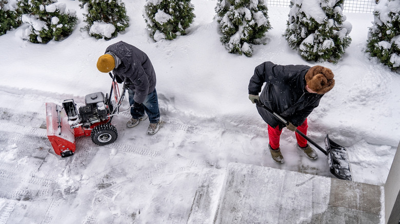 People shoveling and snow blowing driveway