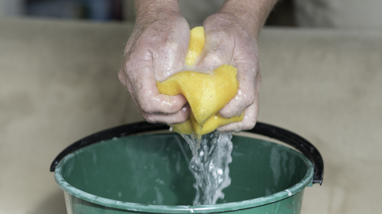 A person squeezes out water from a yellow sponge into a green bucket