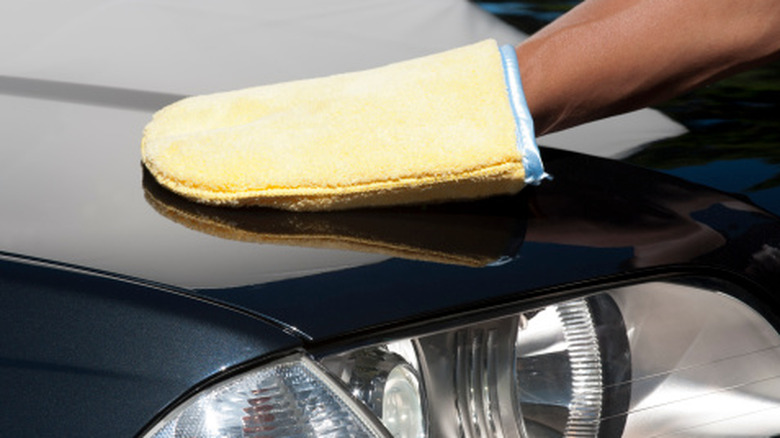 A person polishes a car using a cloth mitten over their hand