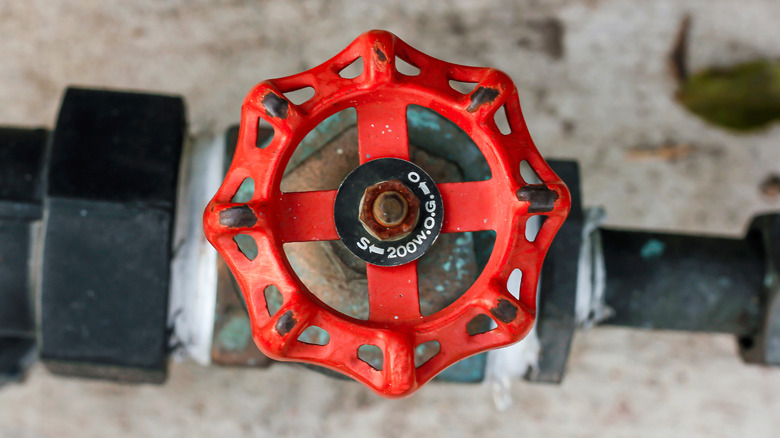 Red water shut-off valve over a stone floor