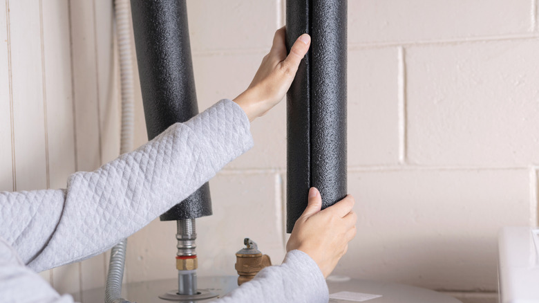 person adding insulation to water heater pipes