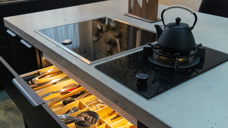 A kettle on a stove installed within a concrete countertop in a kitchen