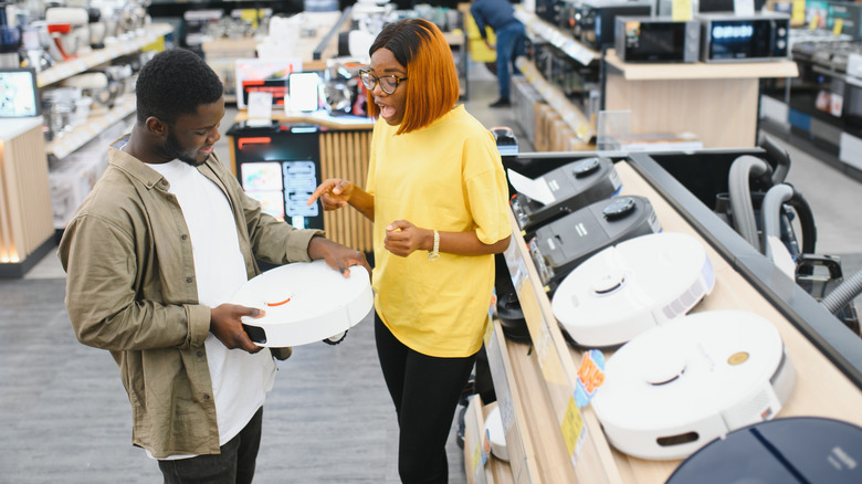 A man and a woman looking at a white robot vacuum cleaner in a store