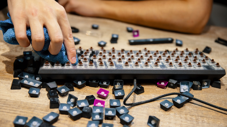 Person cleaning keyboards with removed keys nearby
