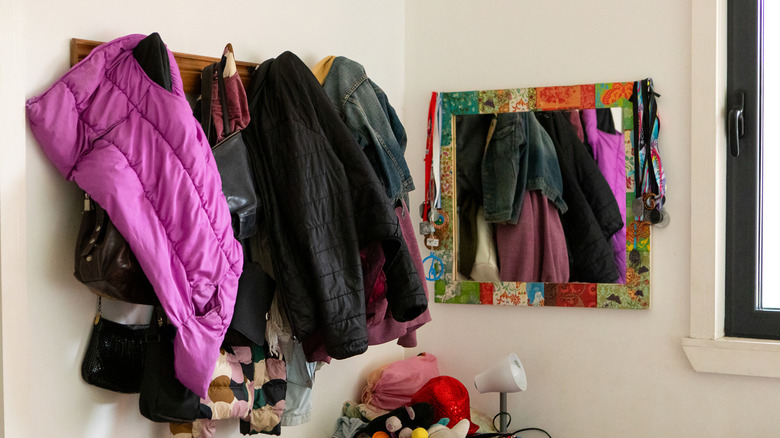 Multiple coats and bags hanging on hooks next to a mirror with a colorful frame.