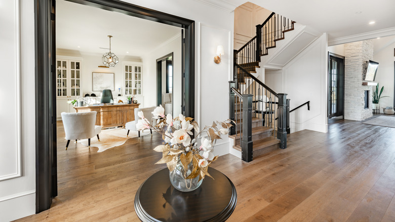 A light, open hallway with wooden floorboards and a small table with a vase of flowers on it in a stylish modern home