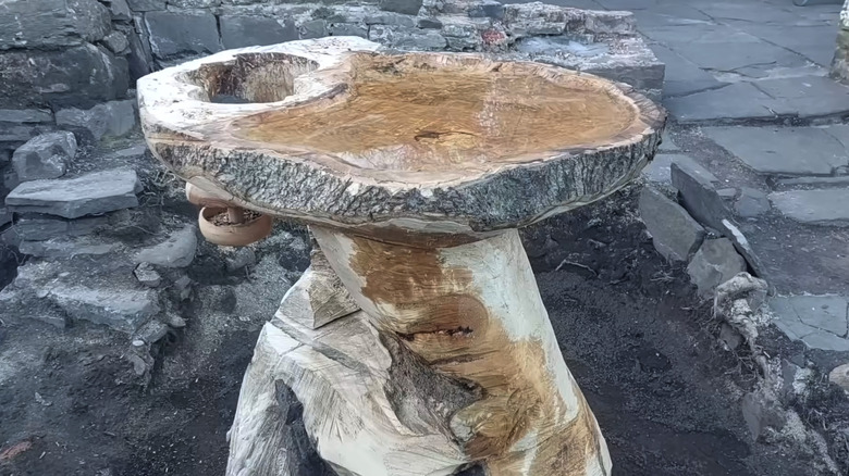 carved tree stump bird bath near a stone path