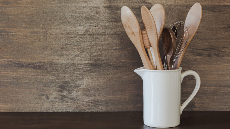 Wooden mixing spoons and utensils stored in a white crock on a counter