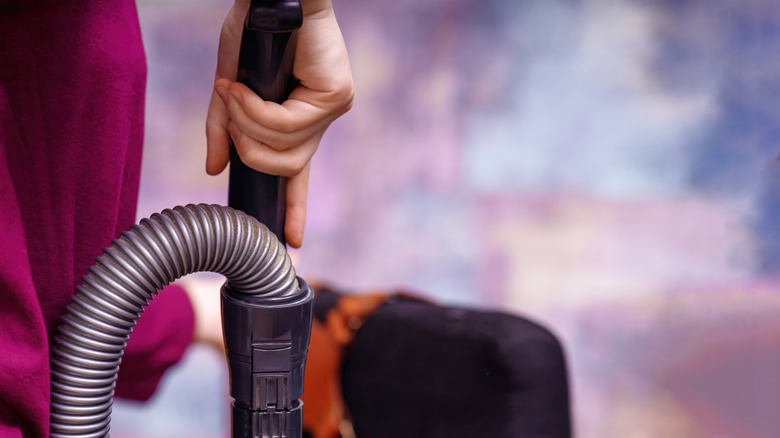 A woman is carrying a vacuum cleaner to do her task