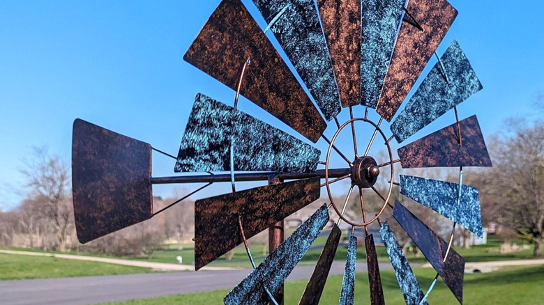 A windmill spinner with a fan and two different copper-esque colors on the grass in a neighborhood