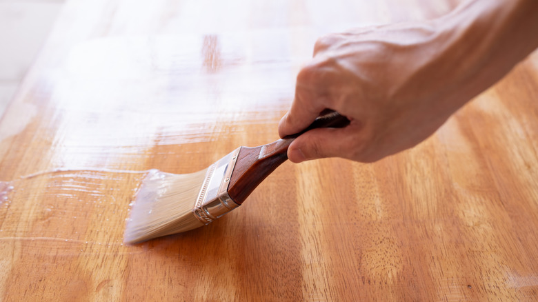 A hand painting a clear top coat on wood.