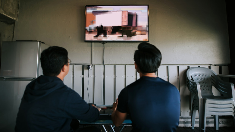 Two men play video games on a tv mounted close to the ceiling