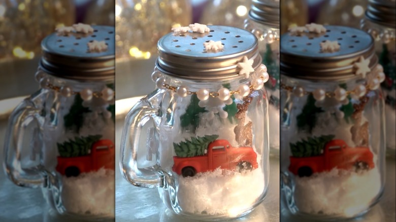 A shaker snow globe filled with craft snow, a reindeer, and a red truck with a tree in the bed.