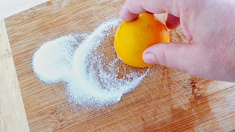 A hand cleans a cutting board with lemon and salt.