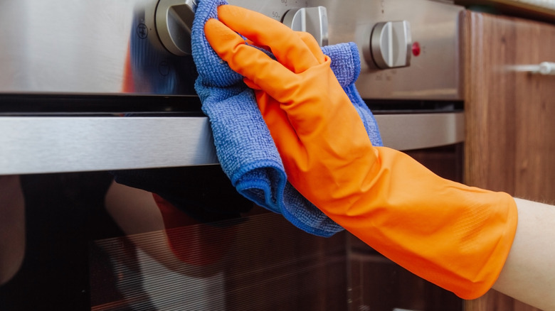 A person is rubbing a microfiber cloth on the outside of an oven