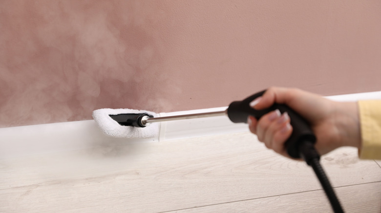 A person cleaning a baseboard with a steam cleaner