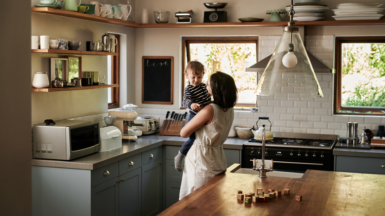 woman holding toddler in a kitchen with dark countertops and white subway backsplash and open shelving