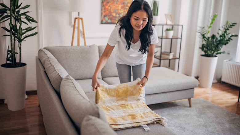A woman folding a blanket on her couch
