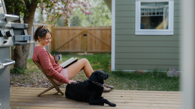 Woman sitting on an outdoor patio on a wooden chair with a black dog next to her