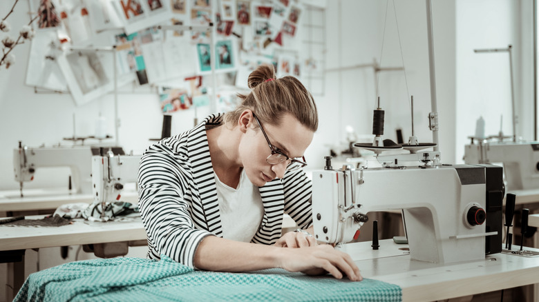 A person stitches some green check fabric using a sewing machine in a craft room.