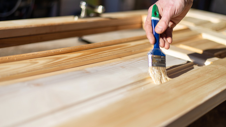 A person using a brush to stain light-colored wood.
