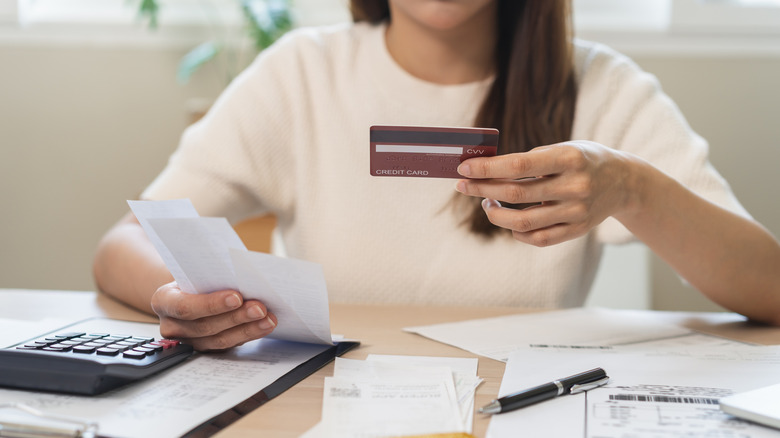 Woman sitting while holding credit card and receipts in front of table with calculator, pen, and documents