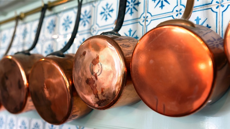 A row of copper pots hang on a blue and white tiled kitchen wall