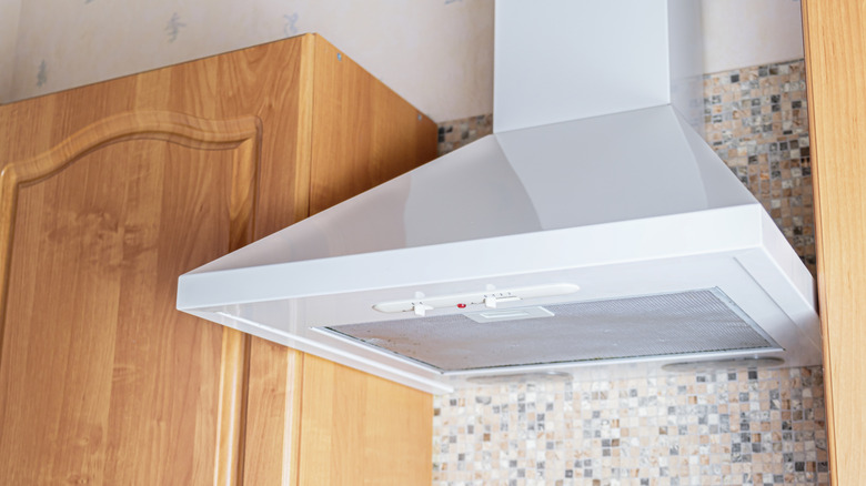 White traditional range hood between oak cabinest with a mosaic backplash and wallpaper