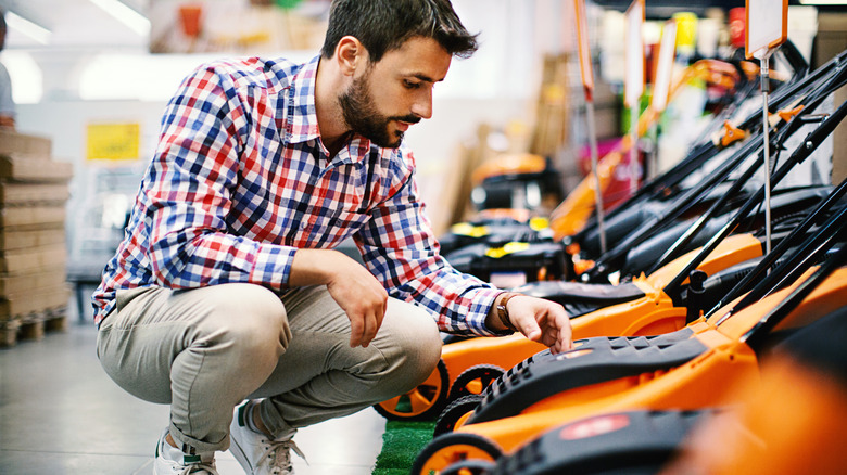 A man crouched down in a store, looking a lawn mowers