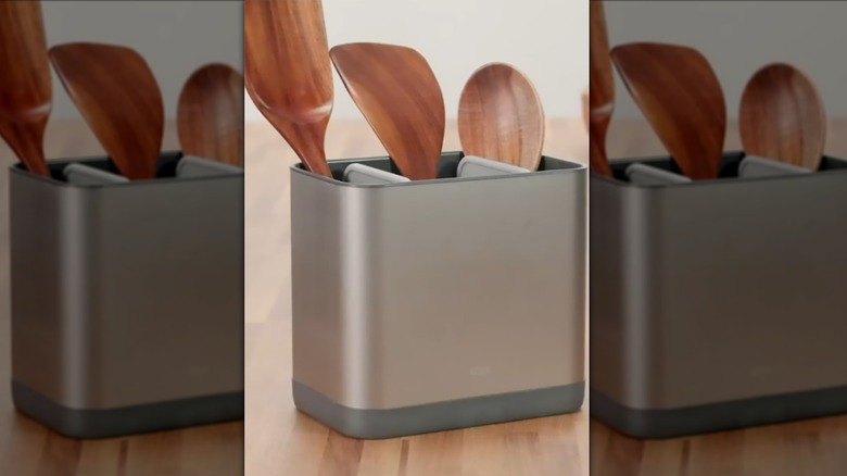 Stainless steel utensil holder containing wooden utensils on wooden surface