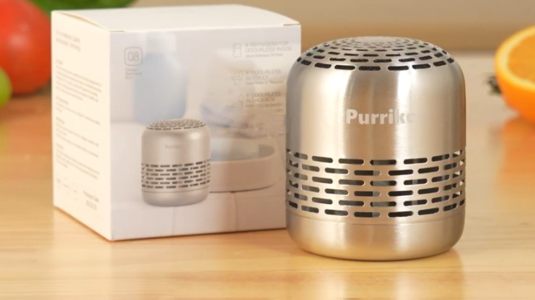 The Purriko Refrigerator Deodorizer sitting on a wooden counter with its box directly behind it and produce in the background